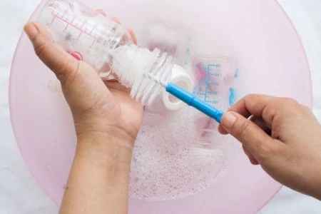 Mother cleaning her baby's bottles using a brush