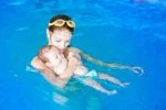 Mother holding baby in the pool wearing swim diapers