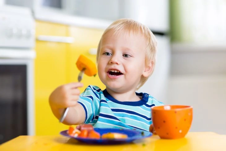 Toddler eating carrots sitting in a hook on high chair
