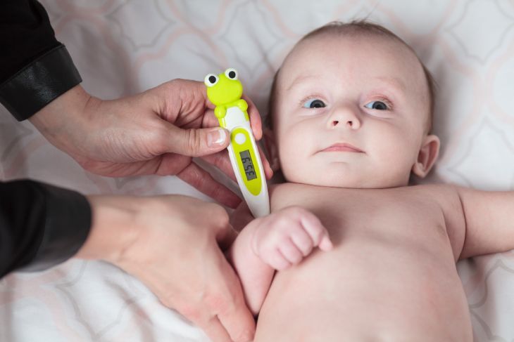 Mother using a baby thermometer to take babys temperature underarm