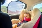 Baby sitting in car seat with sun protection from car sun shade