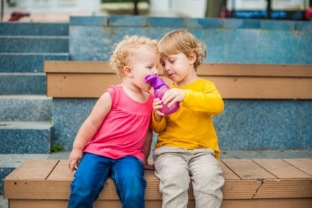 Toddlers drinking water from a reusable water bottle.