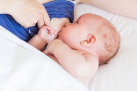 Mother breastfeeding her baby in bed wearing nursing pajamas