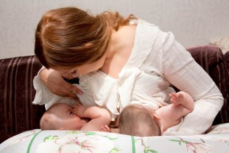 Mother breastfeeding twins using a nursing pillow
