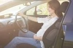 Pregnant woman wearing jeans and driving.