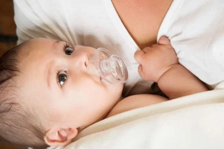 Baby sucking on pacifier waiting to breastfeed