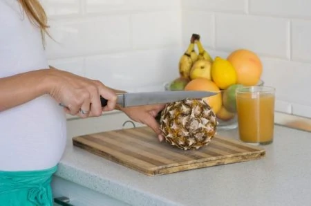 Pregnant woman cutting pineapple
