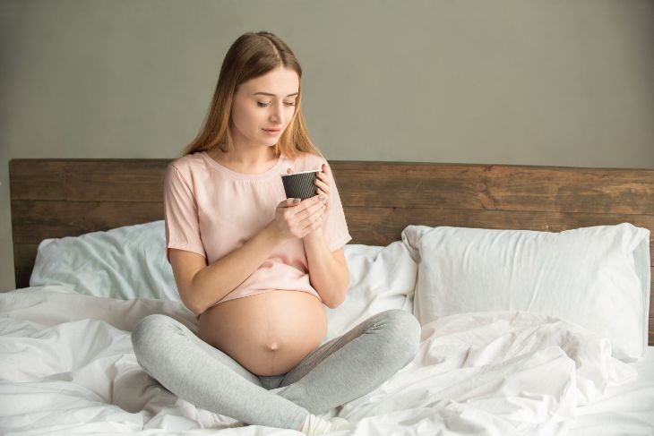 Pregnant woman drinking a cup of coffee in bed