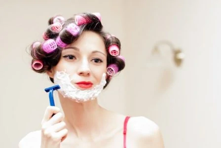 Pregnant woman wearing curlers shaving her face