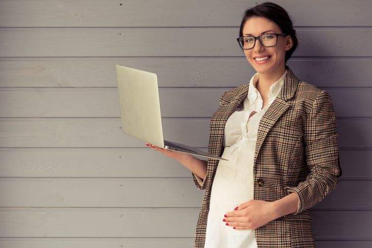 A smiling pregnant woman holding a laptop