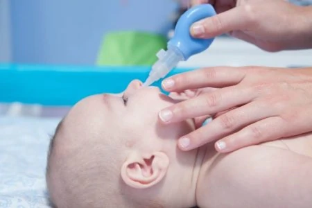 Mother cleaning baby's nose with an aspirator