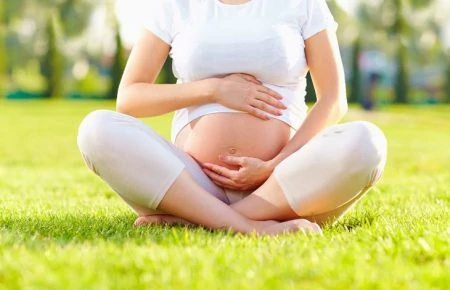 Pregnant woman sitting cross-legged while holding her stomach