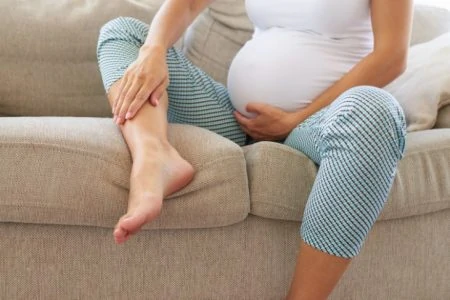 Pregnant woman resting her swollen ankle on the sofa