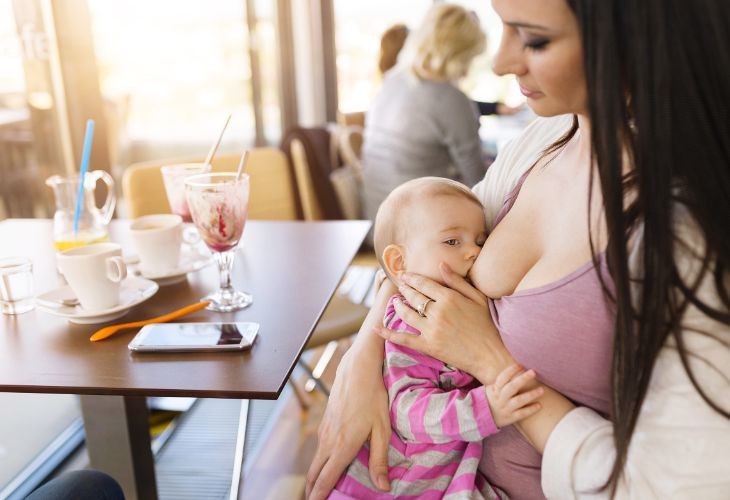 Mom breastfeeding while drinking coffee at coffee shop
