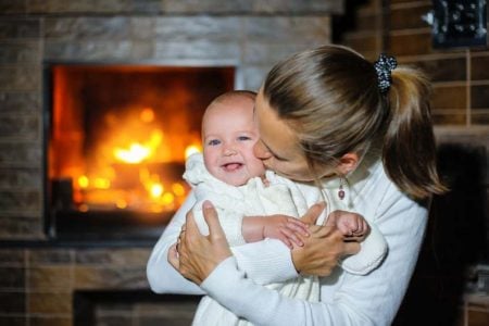 Mother kissing her baby by the fireplace