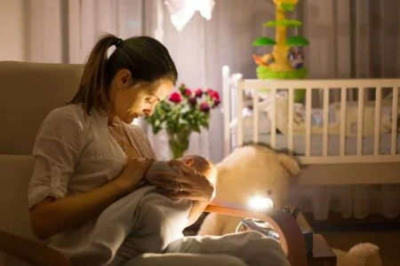 Mother breastfeeding in the nursery with a night light