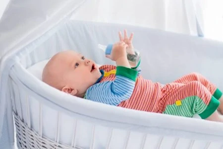 Baby lying inside a bassinet while holding a bottle