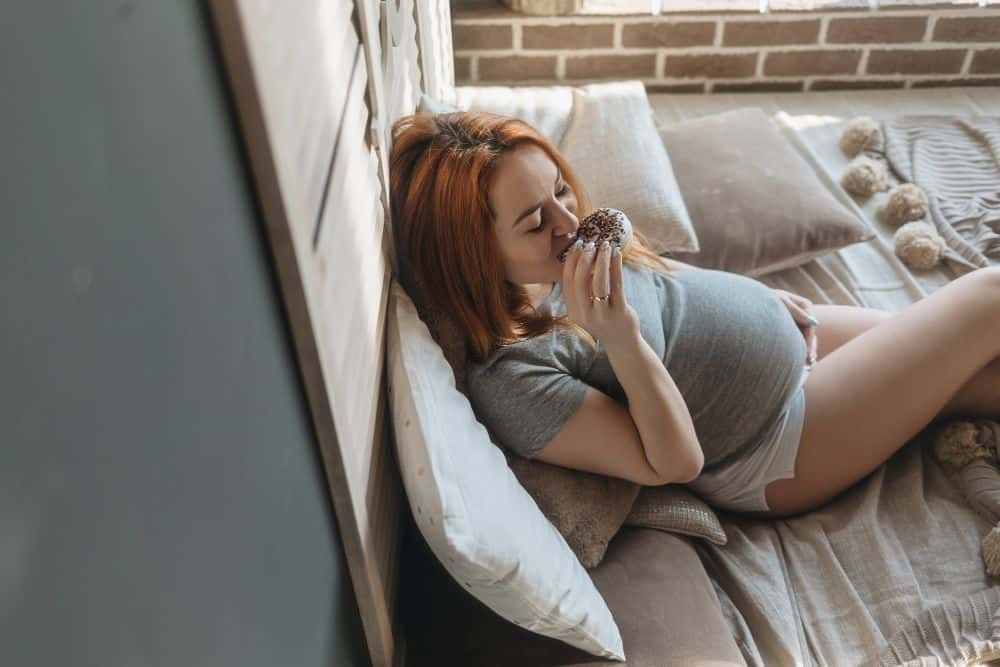Pregnant woman eating a donut on the bed