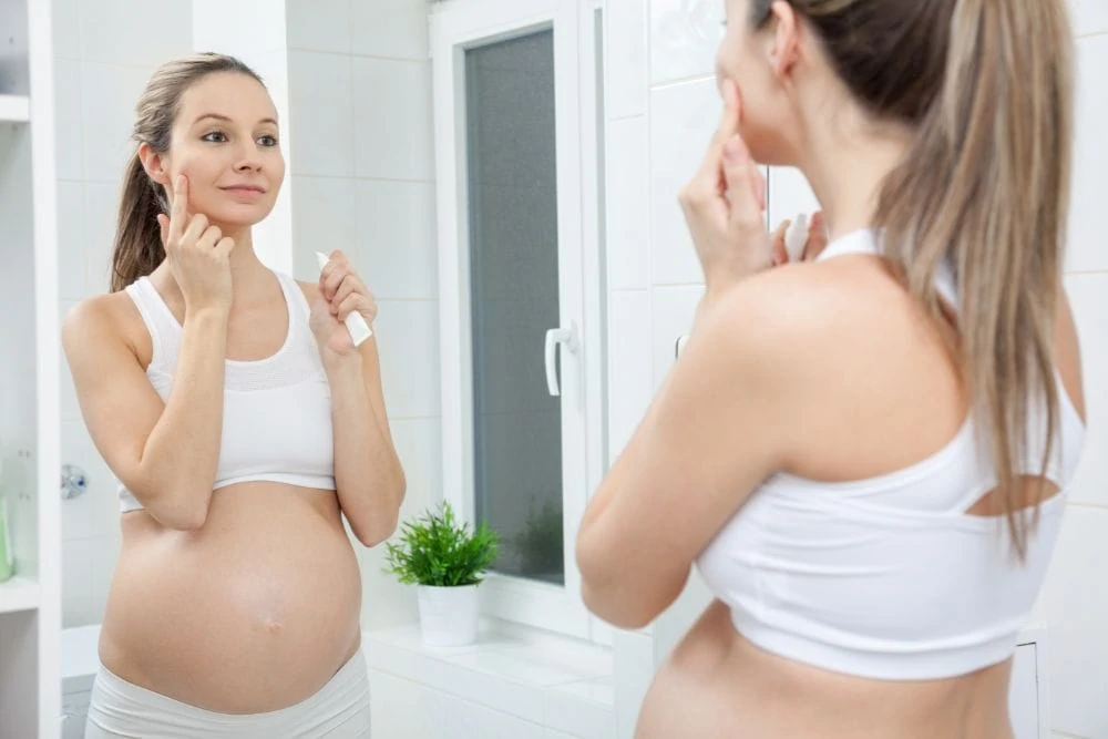Pregnant woman applying skincare product to her face