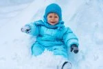 Smiling toddler in a snowsuit playing in the snow
