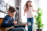 Little boy playing guitar while sister is dancing