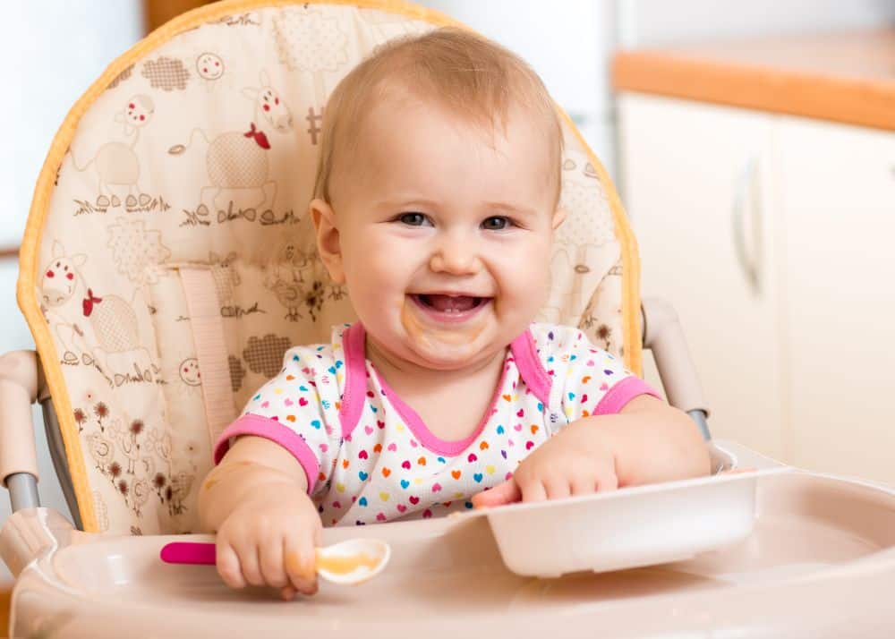 Smiling baby girl eating in a high chair