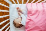 Baby sleeping on a mattress pad with a pink blanket