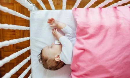 Baby sleeping on a mattress pad with a pink blanket