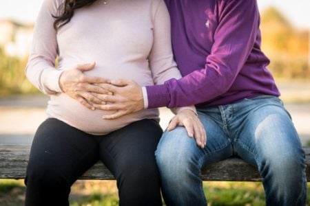 Couple sitting on a bench and holding woman's pregnant belly