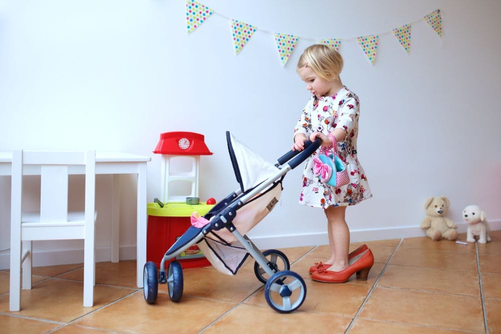 Little girl in heels pushing a doll stroller