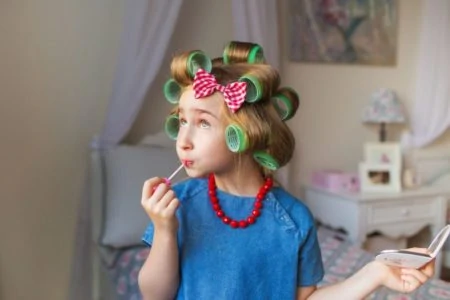 Little girl with hair in curlers putting on lip gloss