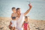 Father playing with RC helicopter at the beach with children