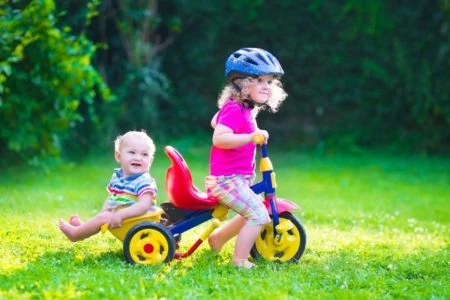 Toddler riding a bicycle with baby brother