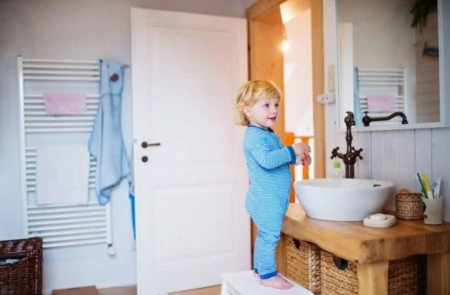 Toddler standing on a stool while brushing his teeth in bathroom
