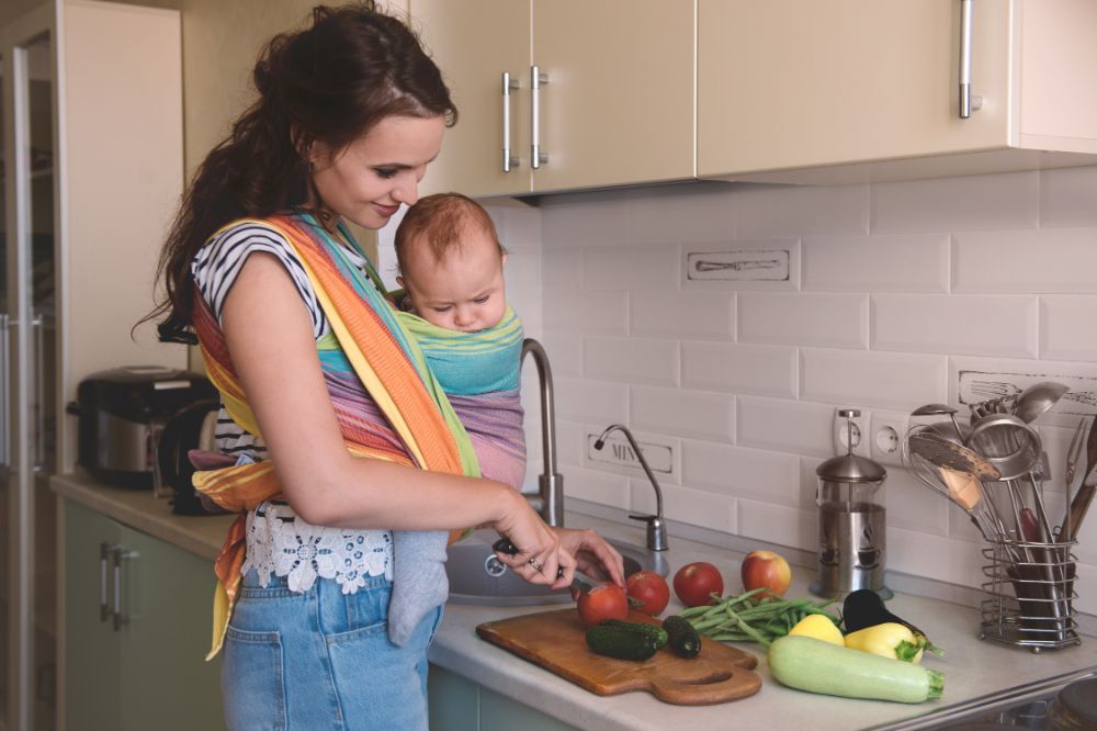 Mom wearing her baby in a carrier while chopping fruits