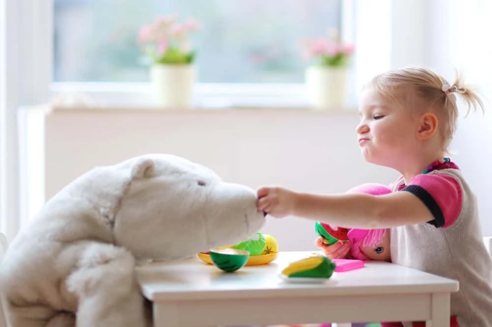 Little girl feeding her stuffed animal toy vegetables