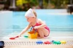 Toddler playing with toy bucket and shovel by the pool