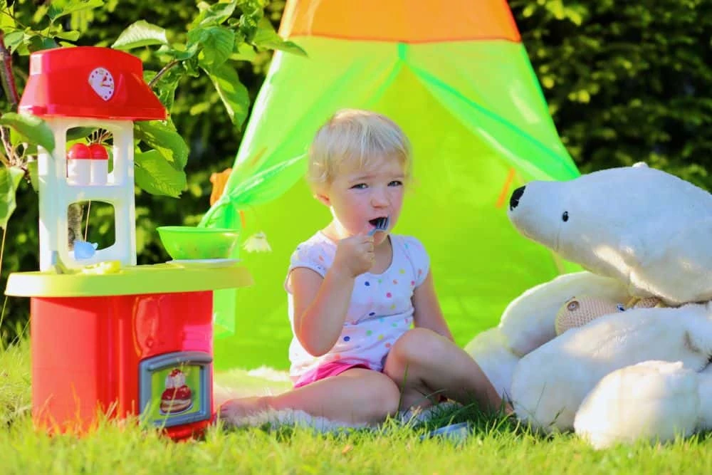Little girl playing outside with stuffed animal and cooking set