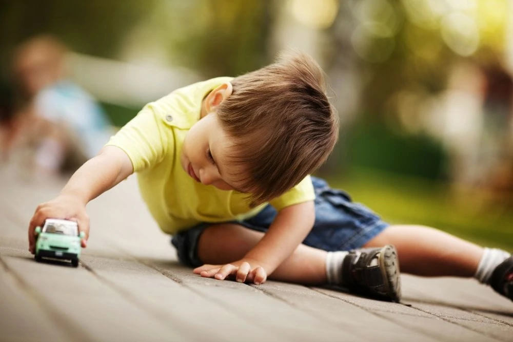 Little boy playing on the ground with a little toy car