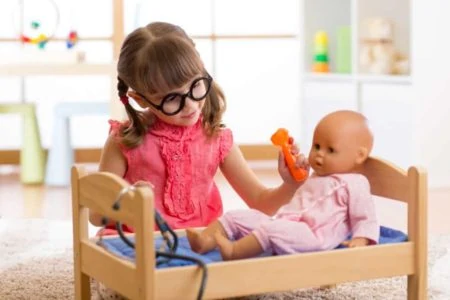 Cute little girl playing doctor with her doll