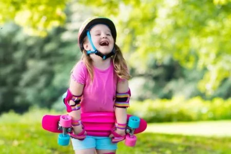 Little girl wearing safety gear while laughing and holding her pink scooter