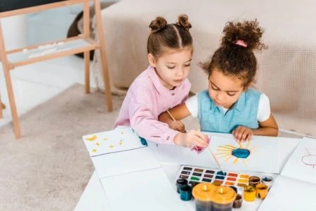 Two young multicultural girls painting on the table