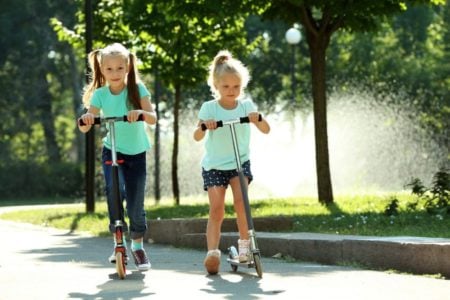 Two young girls in green shirts riding their scooters outdoors