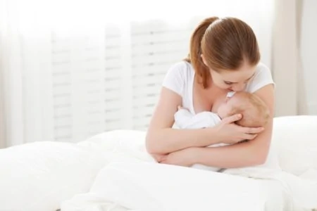 Mother in white holding and kissing her baby in white bed