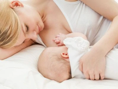 Beautiful blonde mom breastfeeding her baby while laying on her side