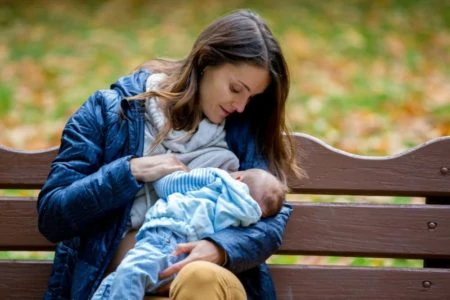 Beautiful mother dressed in warm clothes breastfeeding her baby at the park