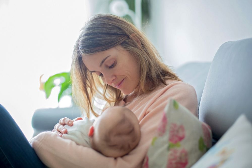 Mother in pink breastfeeding her baby on the couch