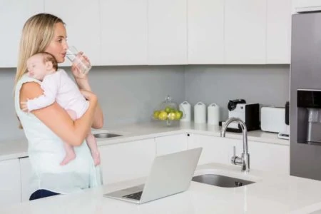 Mom drinking water in kitchen while carrying baby in her arm