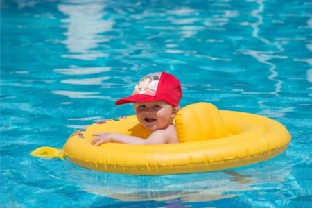 Baby boy in a hat swimming int the pool with a yellow float