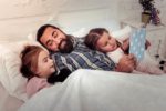 Father reading a book in bed to his two daughters